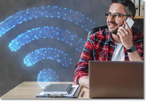 man in a red plaid shirt talking on a cellphone in front of an open laptop with a blue wi-fi symbol next to him made out of lights