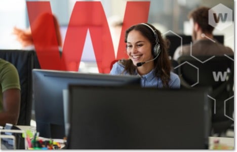 Smiling woman in a headset working in an open office with a large red W behind her