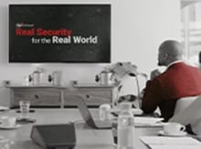 Real Security for the Real World displayed on a wall-mounted tv while a man in a red sweater watches